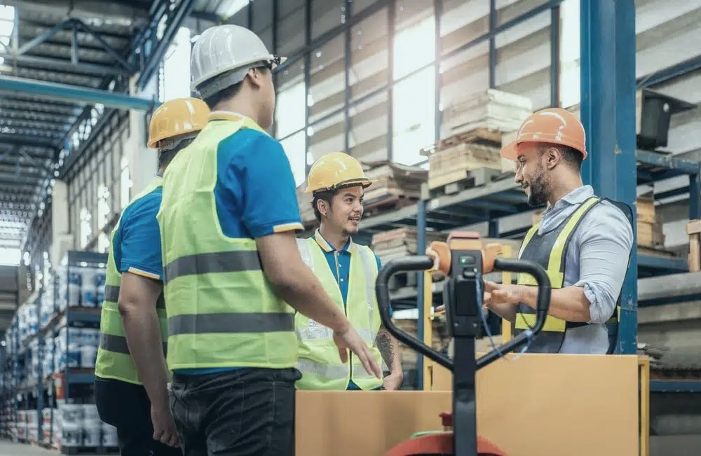Warehouse supervisor briefing a team in hi-vis beside a pallet jack