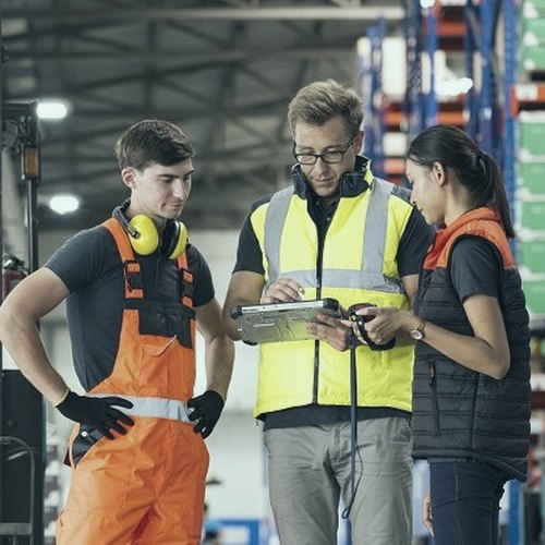 Warehouse team in hi-vis checking a tablet between racking